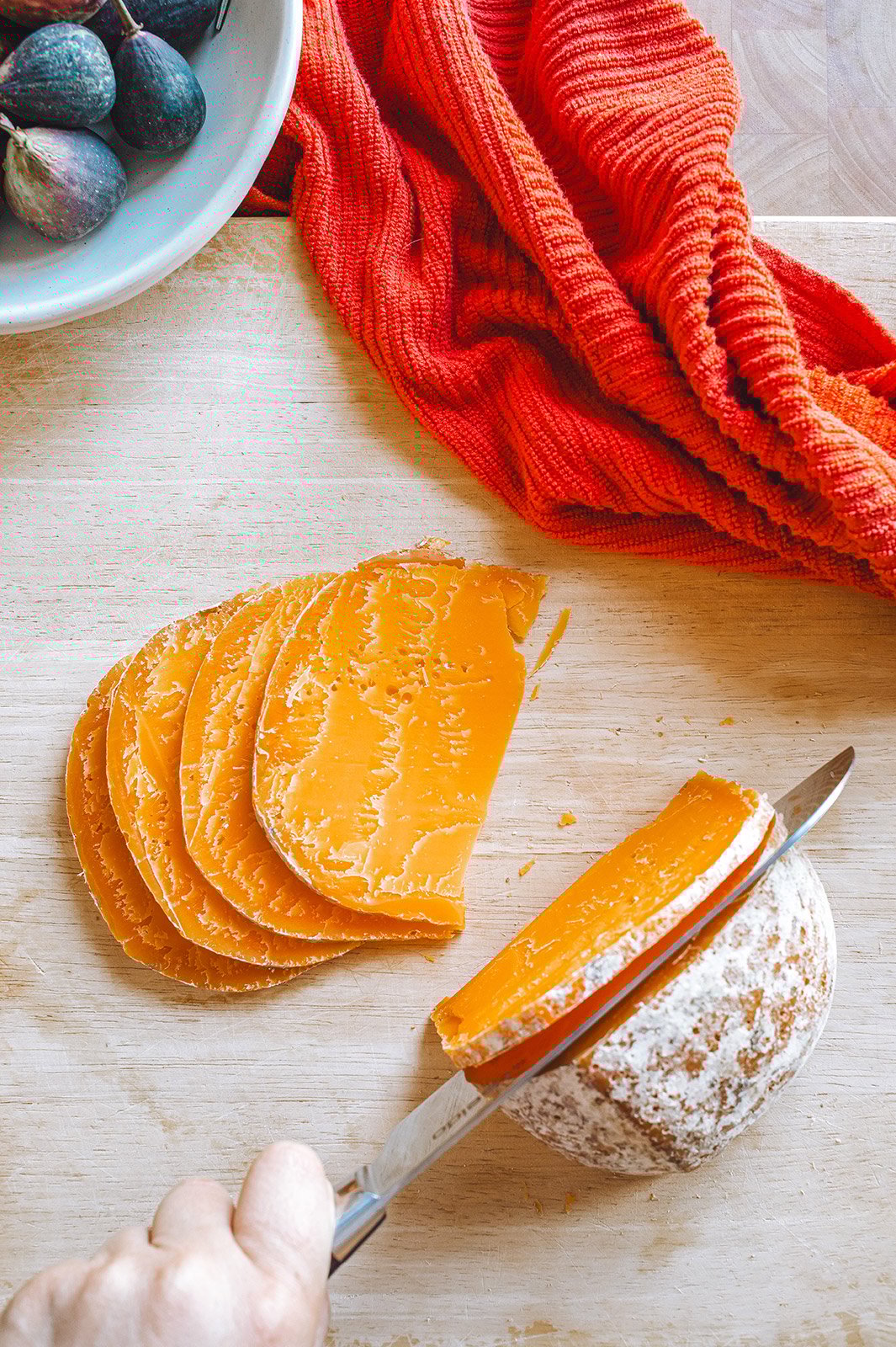 A person's hand cutting a ball of Mimolette cheese on a cutting board
